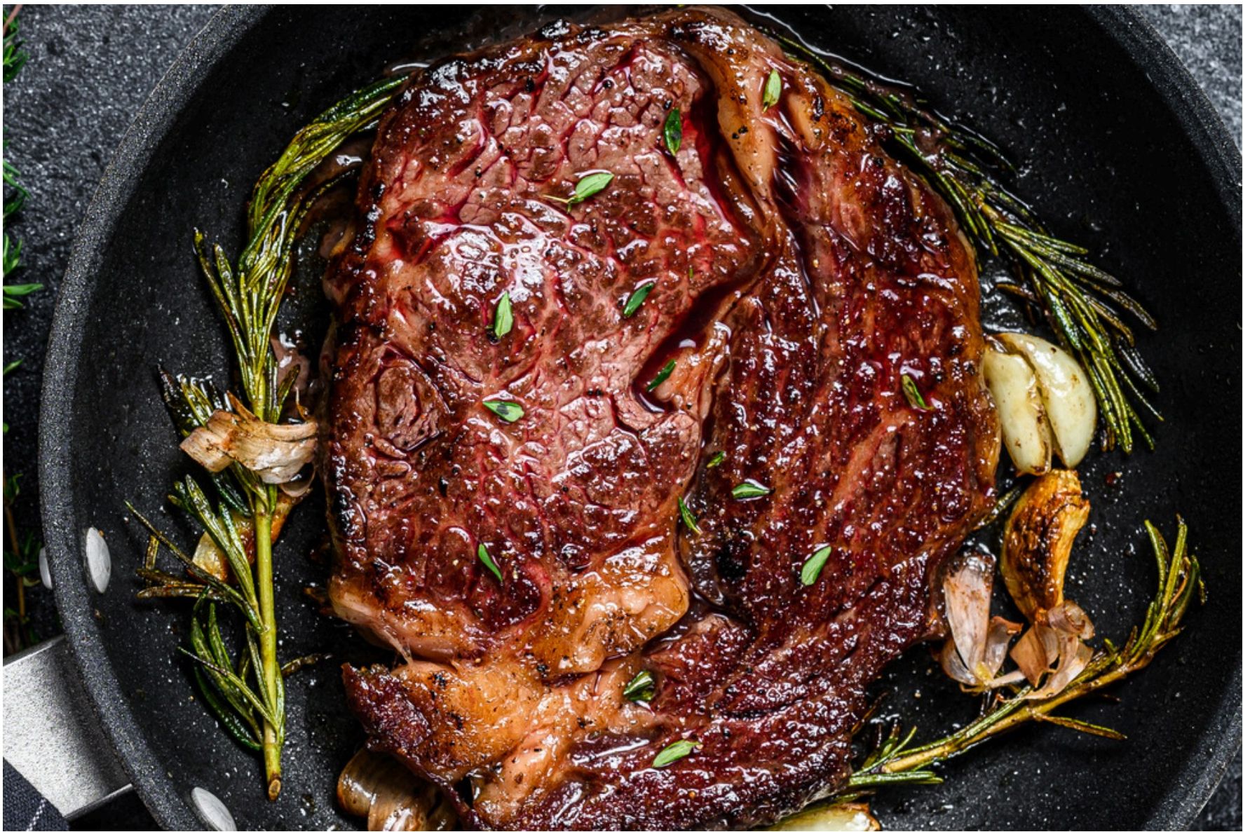 Cooked boneless ribeye steak in a pan with rosemary and garlic