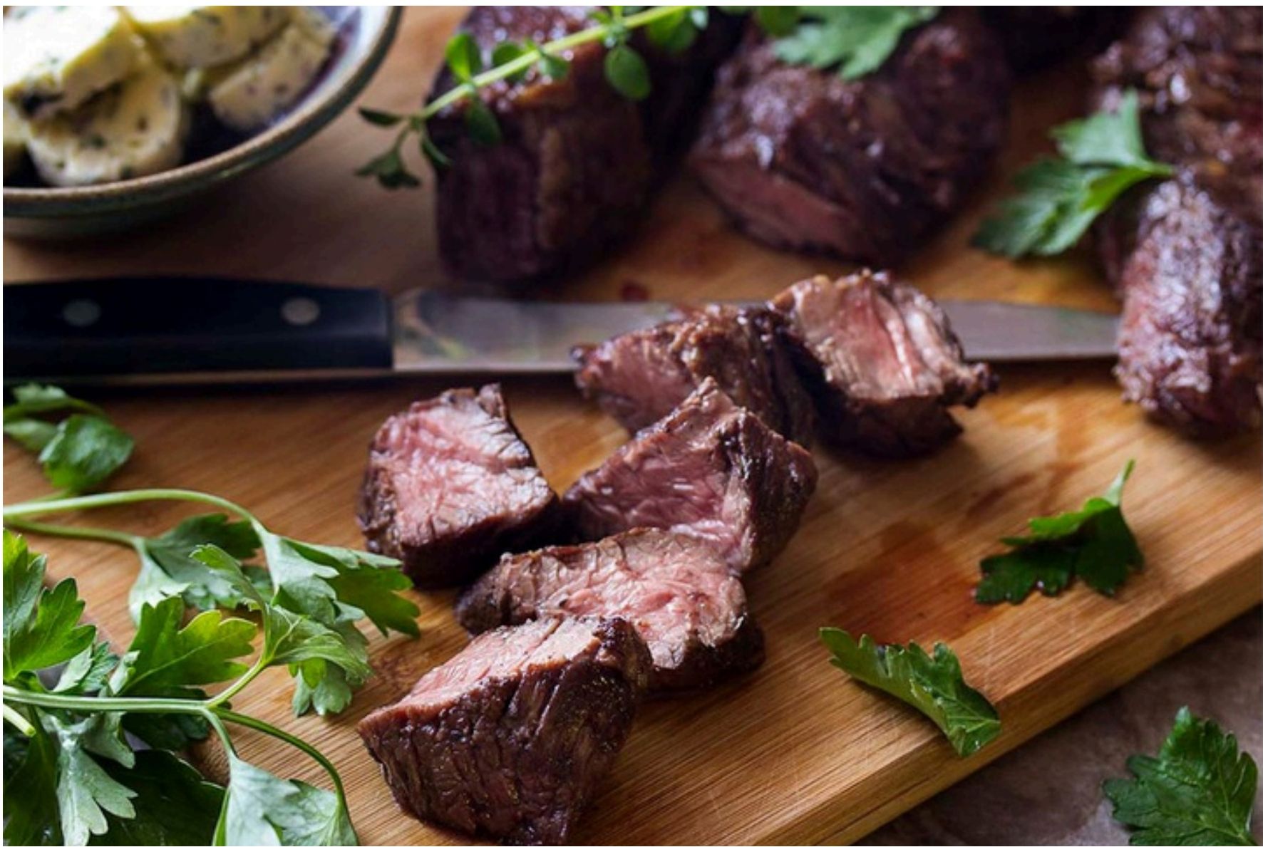 Cooked sirloin tips on a cutting board with herbs and butter